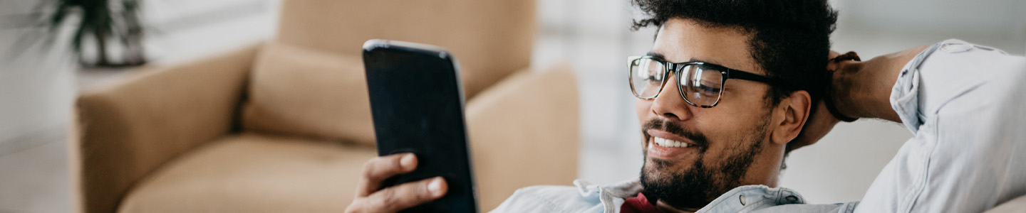 homem negro no sofá com o celular em uma das mãos